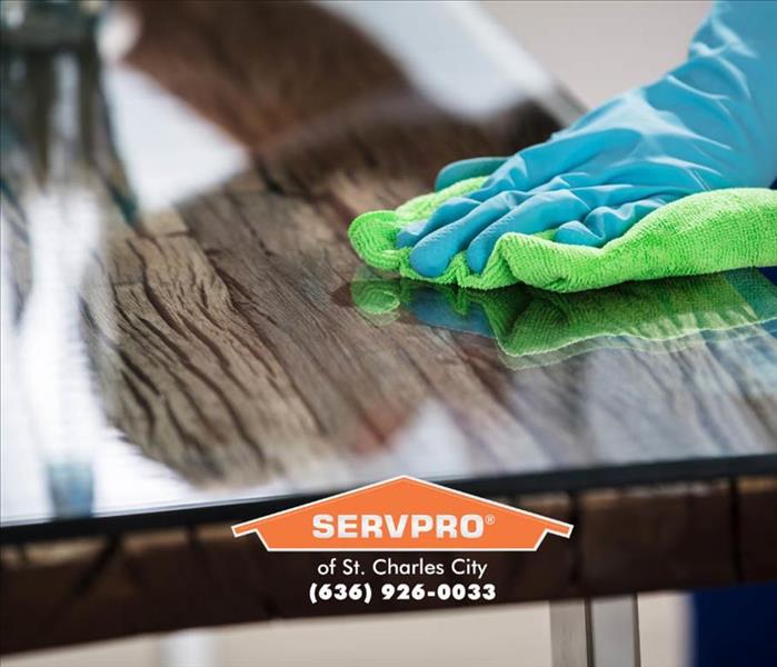 hand in a blue glove wiping a wood table with a green SERVPRO cloth